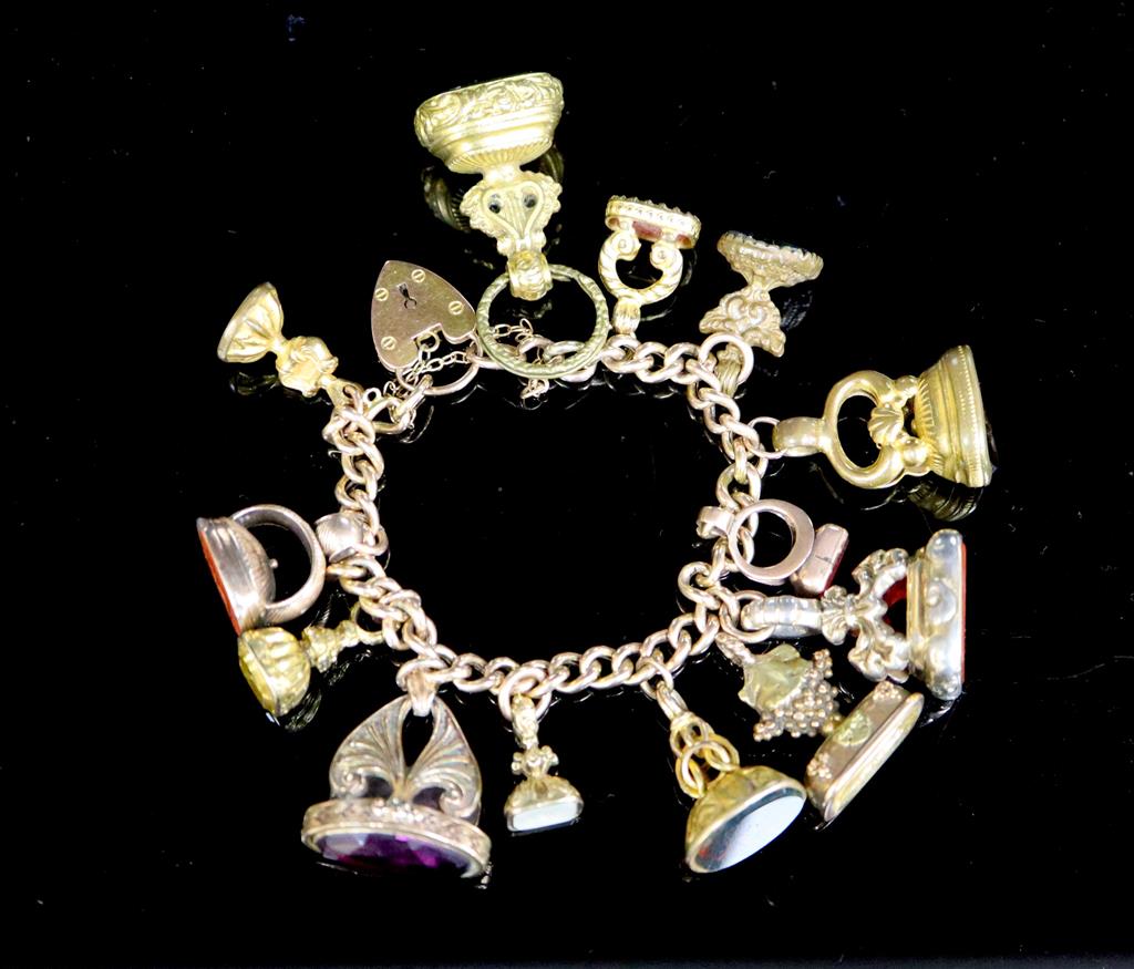 An early 20th century 9ct gold charm bracelet hung with thirteen assorted gold or gilt metal overlaid gem set fob seals,
